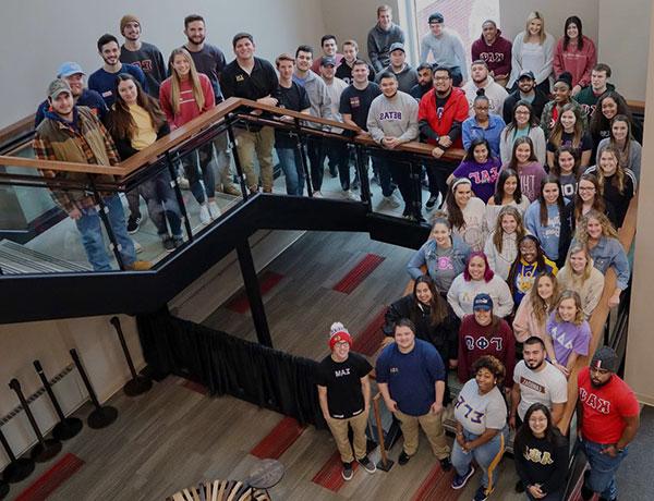 A large group of students wearing greek letters posing in a stairwell.